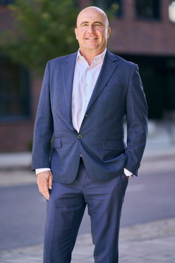 pexels-photo-34129722-34129722 Confident middle-aged businessman in a blue suit smiling outdoors in Bratislava.